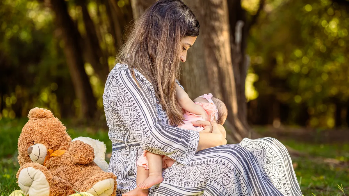 Woman breastfeeding baby while seated on a blanket in a park