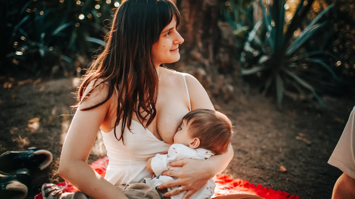 Woman breastfeeding baby while sitting outdoors