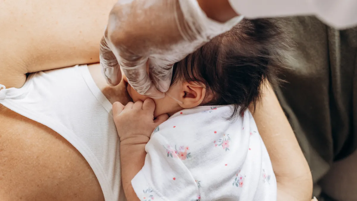 Baby latched at the breast with an assisting hand